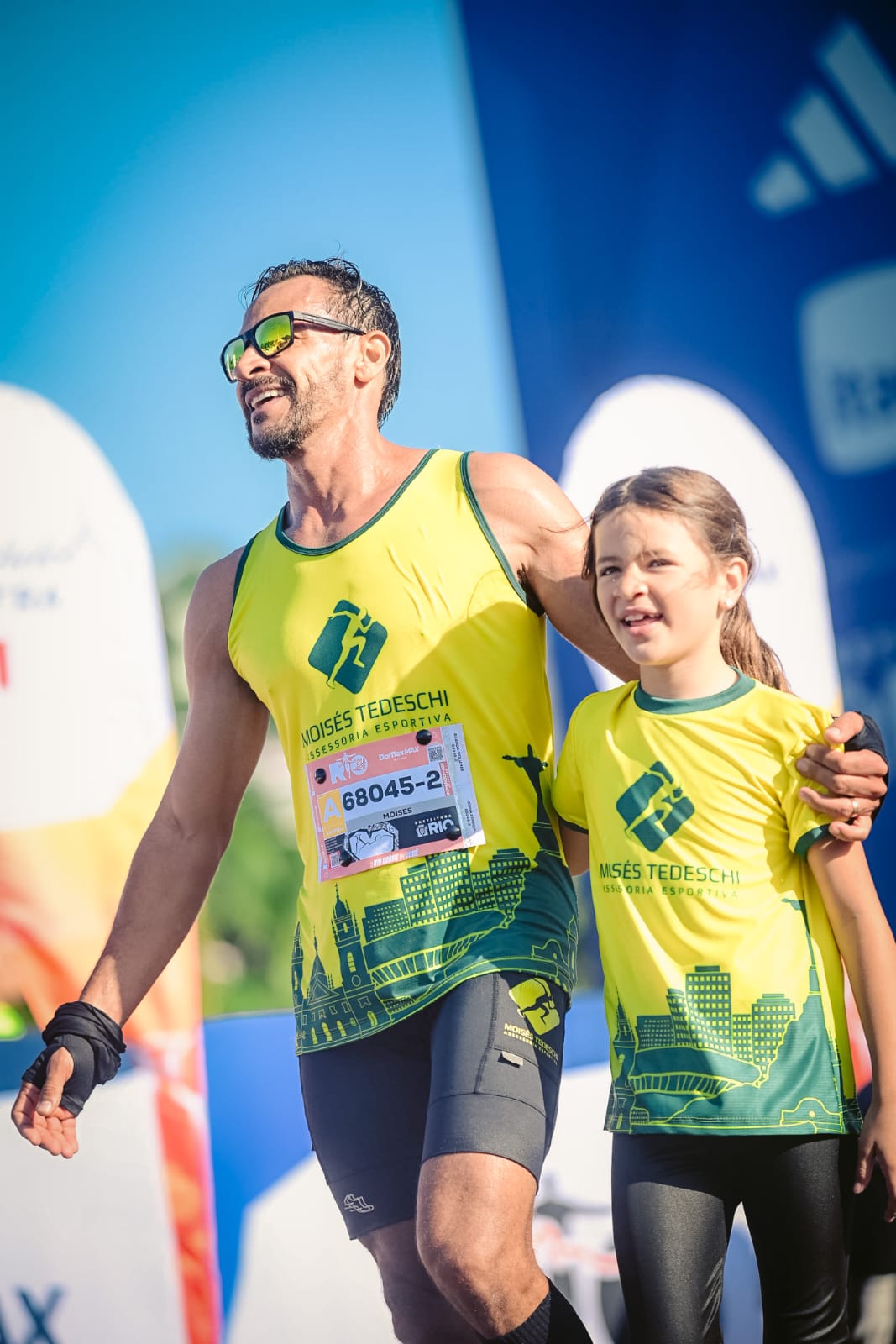 Moisés Tedeschi abraçado com a filha, ambos de uniforme amarelo da assessoria, em prova de corrida